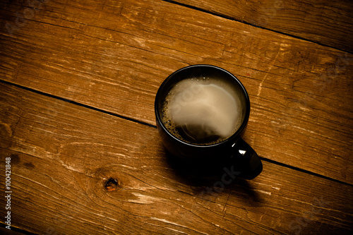 Black cup of coffee on old wooden table. Toned