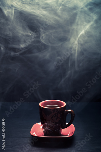 A cup of coffee with smoke on black background. Toned