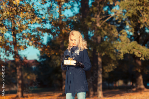 Happy young woman holding a small present box. Happy and positive young blond woman with a gift on outdoor autumn