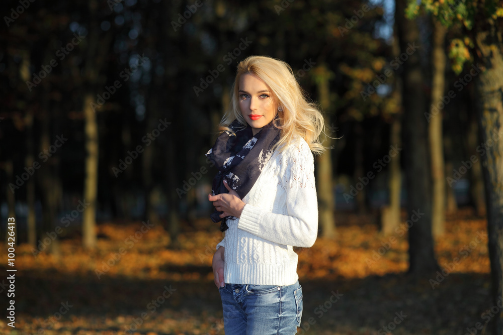 beautiful blonde girl in a white sweater freezing in the autumn park
