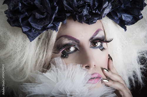 Drag queen with spectacular makeup, glamorous trashy look, posing happily and charming camera from sideways angle