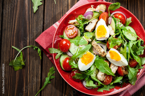 Fresh salad with chicken, tomatoes, eggs and arugula on plate