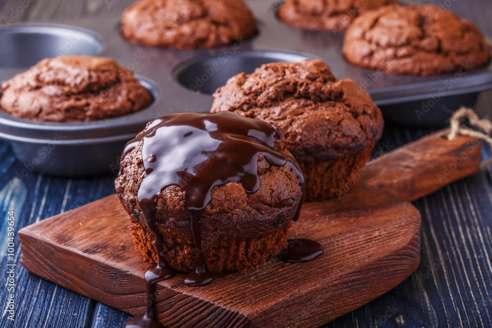 Fototapeta premium Chocolate muffins with chocolate syrup on dark background.