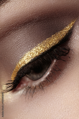 Beautiful macro shot of female eye with ceremonial makeup. Perfect shape of eyebrows, eyeliner and pretty gold line on eyelid. Cosmetics and make-up. Closeup macro shot of fashion sparcle visage
 photo