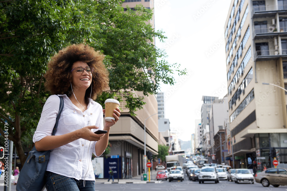 Cheerful woman walking in the city with cell phone