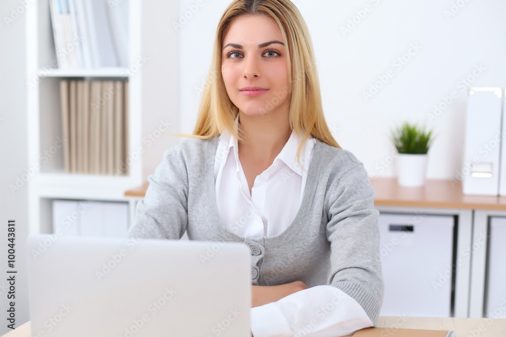 Portrait of young business woman sitting at the desk on office background Portrait of young business woman sitting at the desk on office background