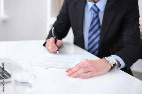 Young business man signs contract sitting at the desk in office