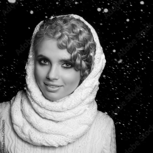 portrait of a beautiful young blonde woman on dark background with snow. hair tied in a braid. girl wearing a warm sweater and scarf. copy space. photo