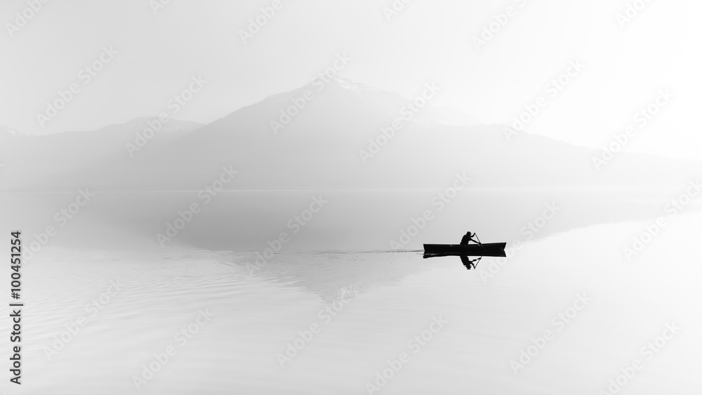 Obraz premium Mgła nad jeziorem. Sylwetka gór w tle. Mężczyzna unosi się w łodzi z wiosłem. Czarny i biały