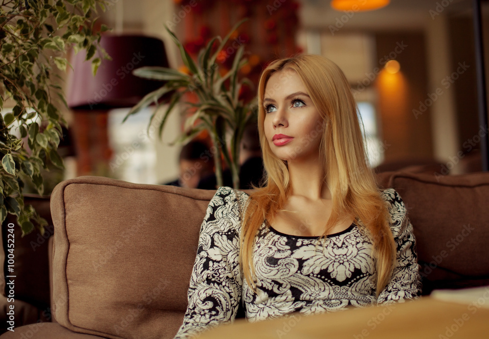 Portrait of a cute blonde smiling woman sitting in a cafe with a cap of coffee Portrait of a cute blonde smiling woman sitting in a cafe with a cap of coffee