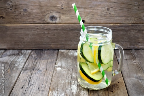 Lemon cucumber detox water in a mason jar glass with straw against a rustic wood background
