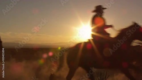 Cowboys galoping past the camera in slow motion during a golden sunrise sunset. photo