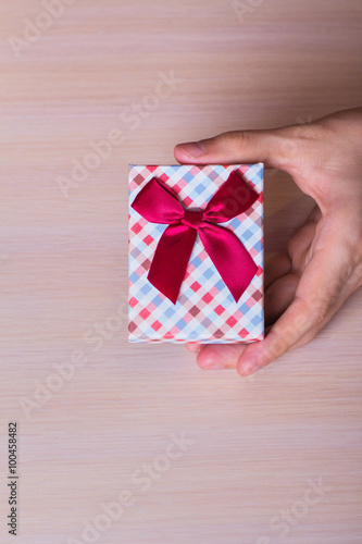 One male hand holding checkered gift box with vinous bow