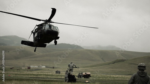 Shot from field of Black Hawk helicopter and soldiers preparing to haul off cargo.