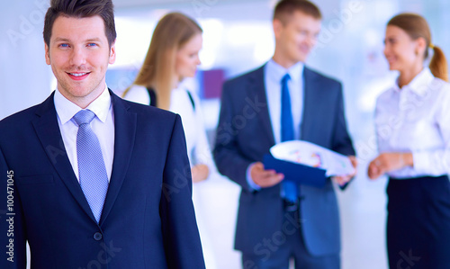 Portrait of young businessman in office with colleagues in the background