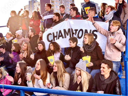 Sport fans holding banner with writting champion and singing on tribunes. Group people.