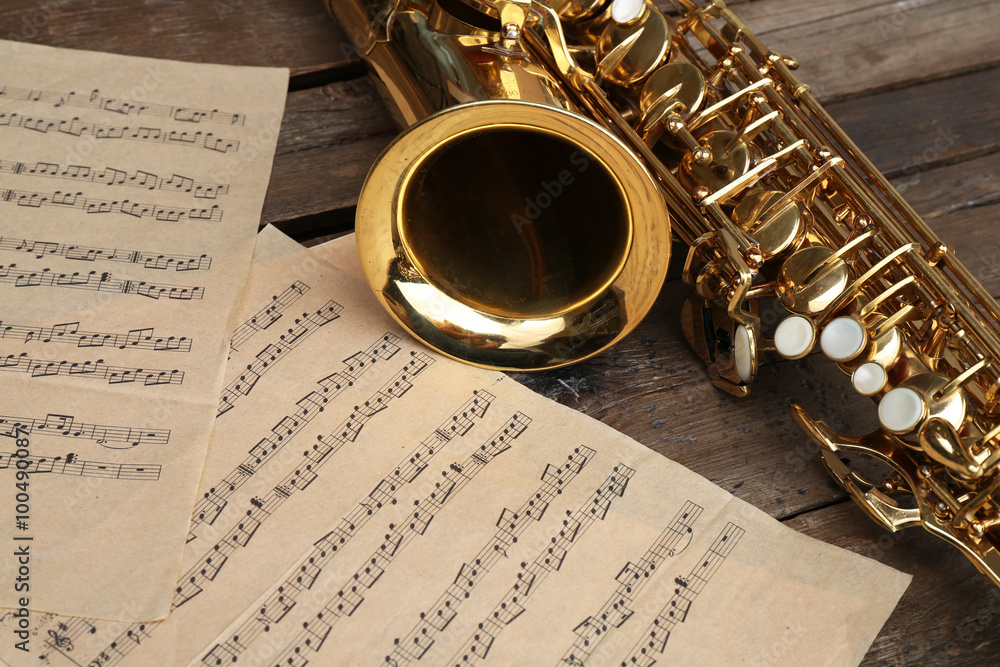 Naklejka premium Beautiful golden saxophone with musical notes on wooden background, close up
