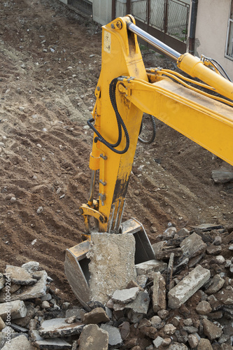 Yellow excavator digs dirt, asphalt and gravel on construction site. Motion blur.