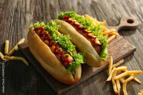 Delicious hot-dogs with French fries on wooden chopping board