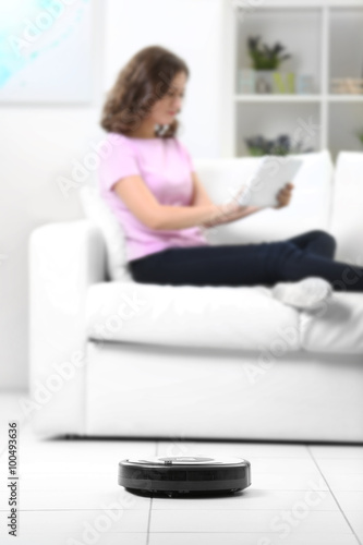 Cleaning concept - automatic robotic hoover clean the room while woman relaxing with tablet, close up