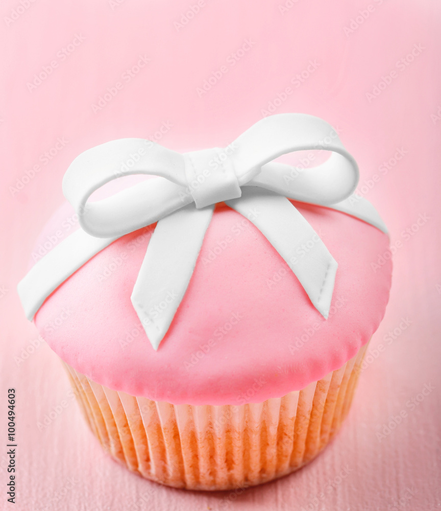 Tasty cupcake with bow on color wooden background Tasty cupcake with bow on color wooden background