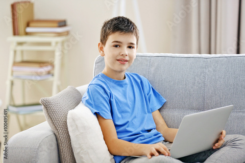 Boy with laptop sitting on a sofa at home