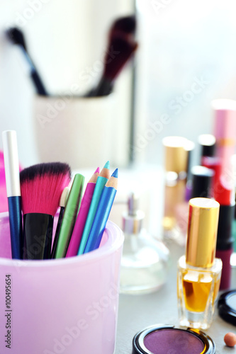 Makeup pencils, brush with cosmetics on a table, close up