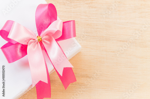 Pink ribbon bow and white gift box on wooden background.