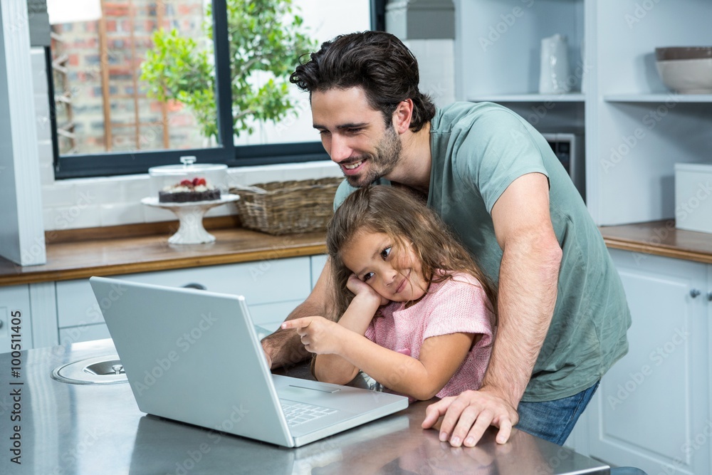 Smiling father and daughter using laptop in the kitchen Smiling father and daughter using laptop in the kitchen