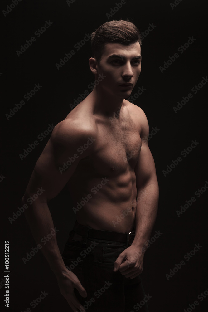fit handsome man side posing in dark studio background while fle