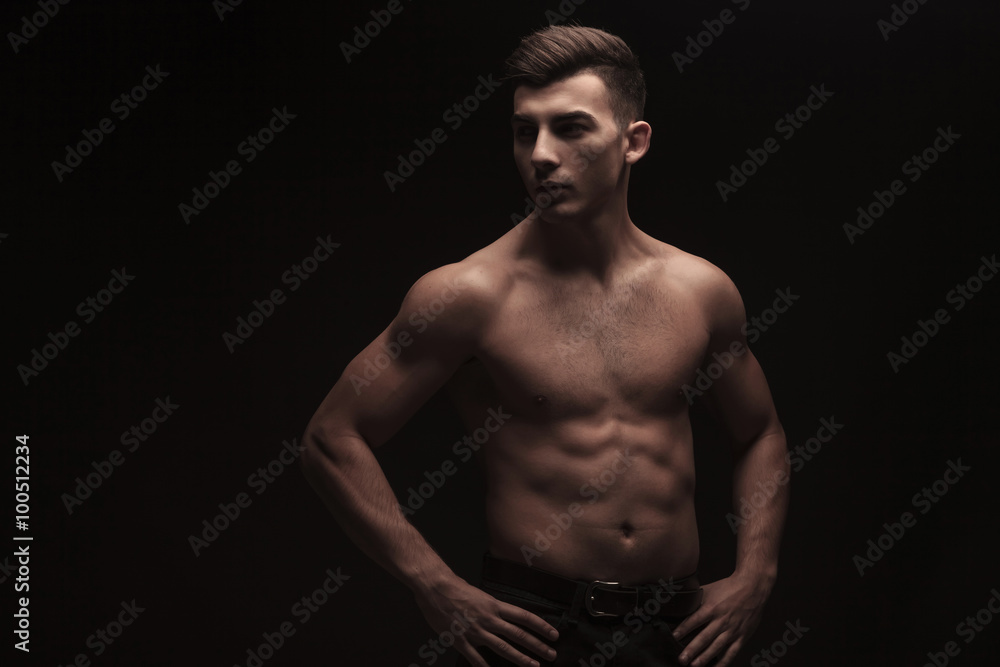 fit young man posing in dark studio background with hands on wai
