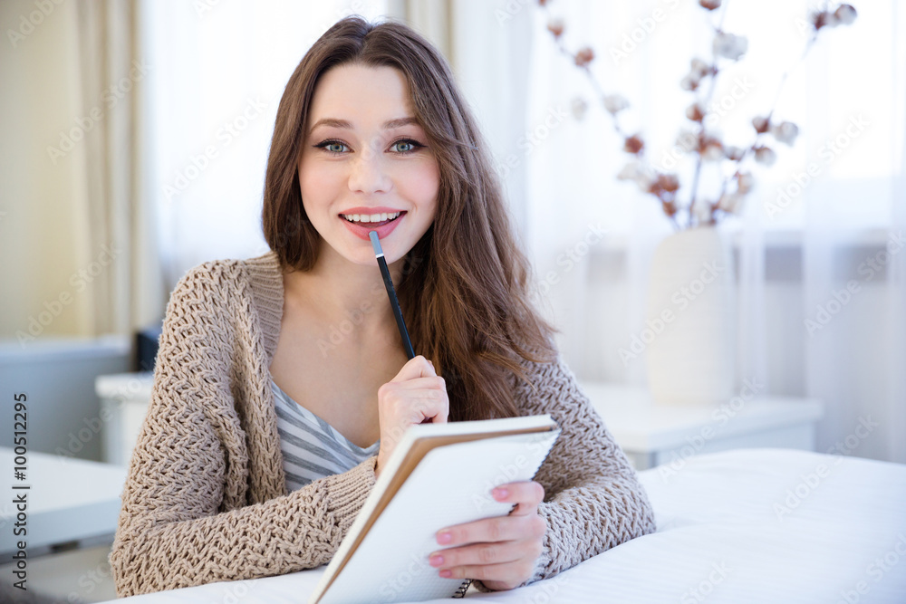 Charming cheerful young woman thinking and writing in notepad Charming cheerful young woman thinking and writing in notepad