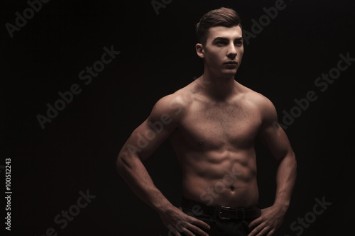 young male flexing in dark studio background with hands on waist