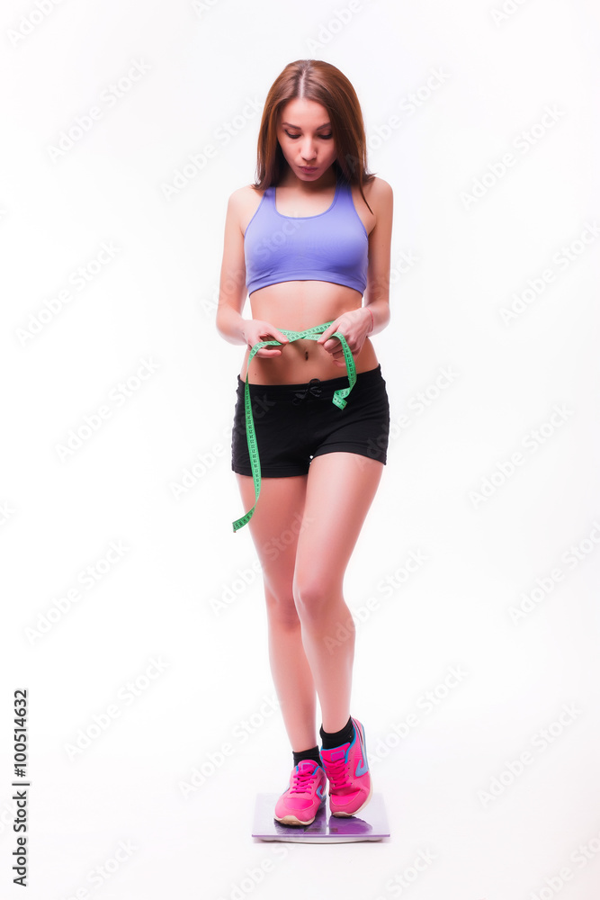 Fit and healthy young lady measuring her waist with a tape measure in centimeters and millimeters. Isolated image on white. Fit and healthy young lady measuring her waist with a tape measure in centimeters and millimeters. Isolated image on white.