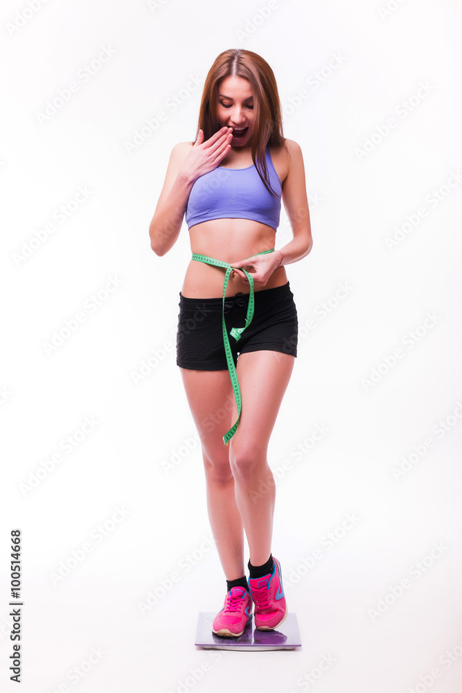 Fit and healthy young lady measuring her waist with a tape measure in centimeters and millimeters. Isolated image on white. Fit and healthy young lady measuring her waist with a tape measure in centimeters and millimeters. Isolated image on white.