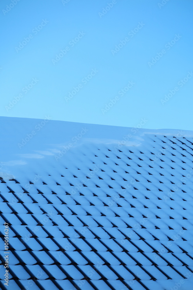 Modern roof covered with tile effect PVC coated metal roof sheets with snow against a blue sky Modern roof covered with tile effect PVC coated metal roof sheets with snow against a blue sky