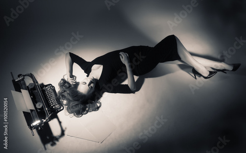 Fotografi Young woman in black dress lies near a typewriter.