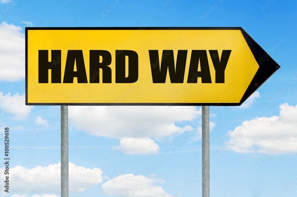 Hard way Sign -Yellow road sign with arrow pointing right against blue cloudy sky Hard way Sign -Yellow road sign with arrow pointing right against blue cloudy sky