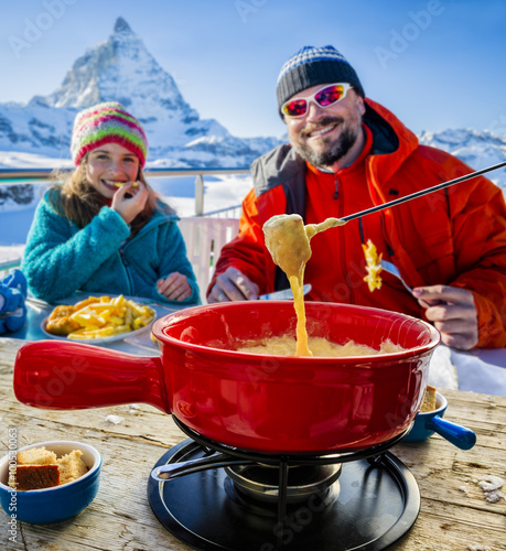 Skiers in a restaurant, Fondue, traditional Swiss dish - Matterhorn in Swiss Alps in background