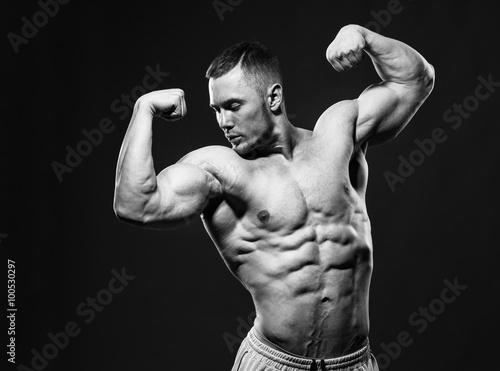 Muscular shirtless man in studio over dark background shows his muscles. © chettythomas