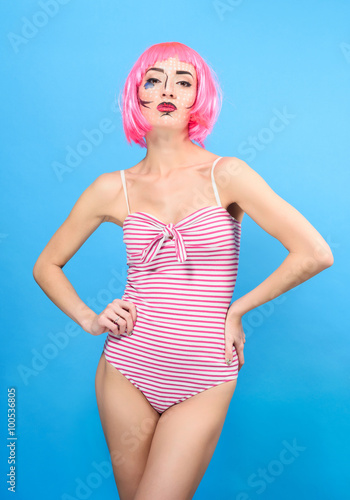 Young woman with creative pop art make up and pink wig looking at the camera on blue background