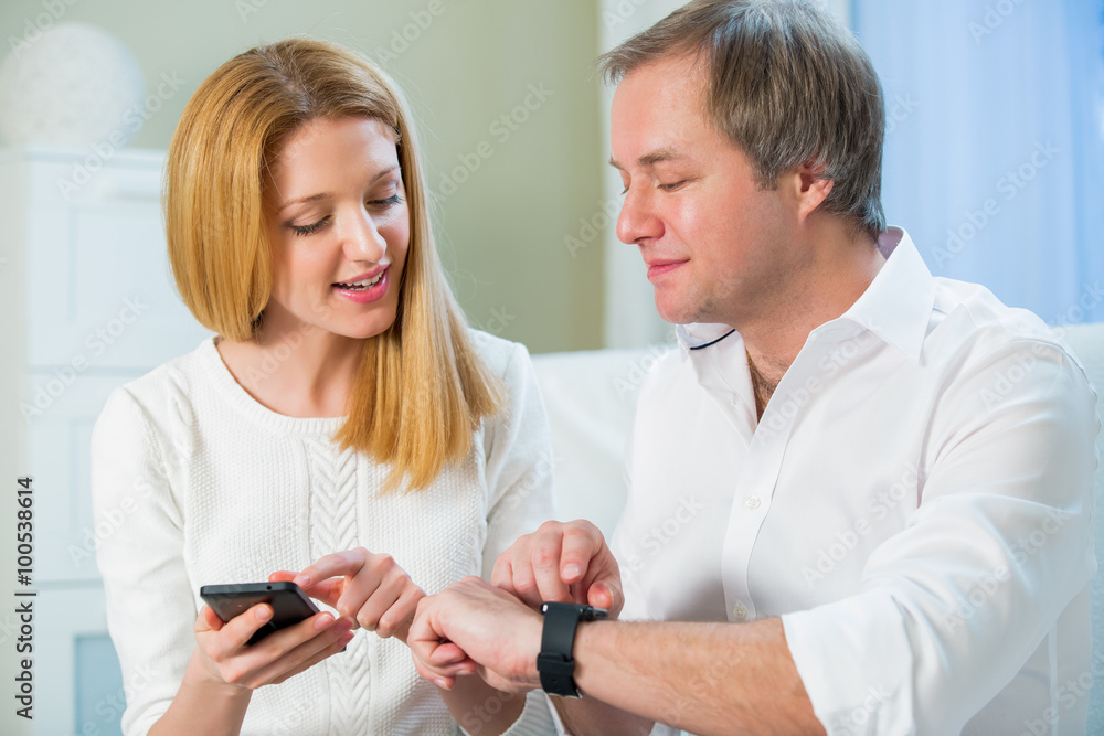 Woman and Man in white shirt sitting on the sofa and looking at smart watch. Showing how to use and synchronizing with smart phone
Woman and Man in white shirt sitting on the sofa and looking at smart watch. Showing how to use and synchronizing with smart phone