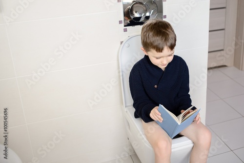 Boy sitting on the toilet and reading a blue book