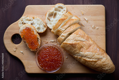 Sliced baguette and red caviar on a wooden cutting board