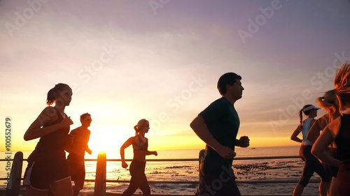 Running club running along sea promenade in the sunset. Young people running on the road along the sea in evening. 

