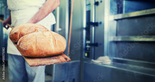 Bäcker mit Brot in Bäckerei auf Schaufel steht vor dem Backofen