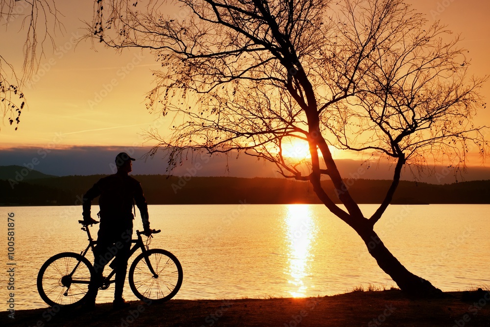 Young man cyclist silhouette on pink orange sky and sunset background on the beach.