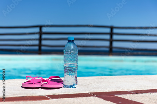 Plastic bottle with pure water and slippers near swimming pool