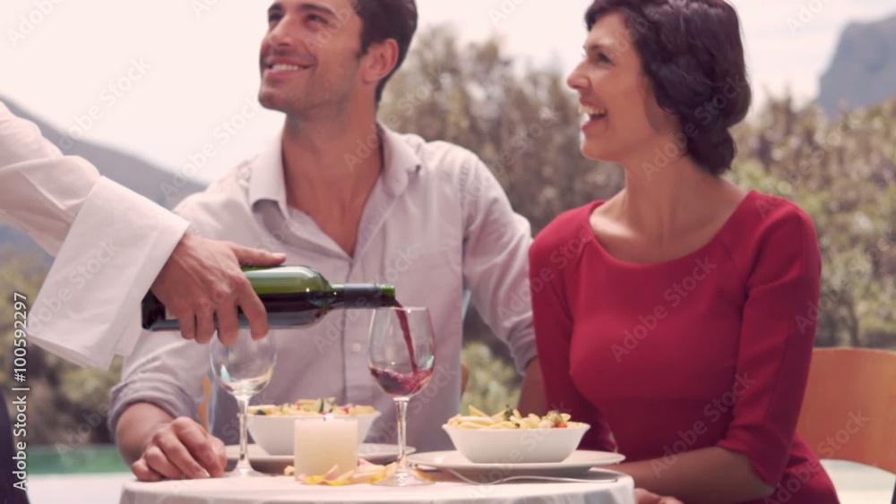 Waiter pouring red wine in glass for couple Waiter pouring red wine in glass for couple