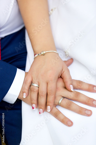 Руки жениха и невесты с серебряными обручальными кольцами одна на другой